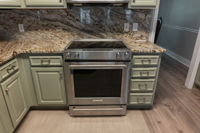 kitchen with tasteful backsplash, dark stone counters, light hardwood / wood-style flooring, high end range, and green cabinetry