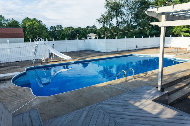 view of swimming pool with a wooden deck, a water slide, and a pergola