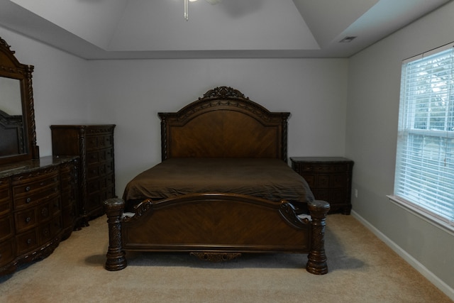 bedroom with a raised ceiling and light colored carpet