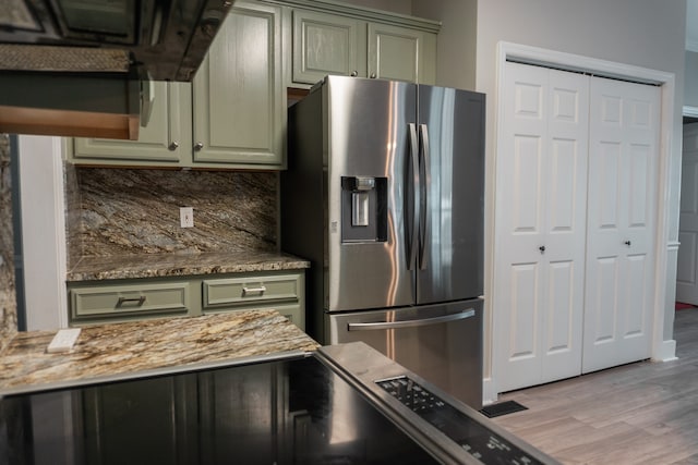 kitchen featuring stainless steel fridge, green cabinets, stone counters, and light wood-type flooring