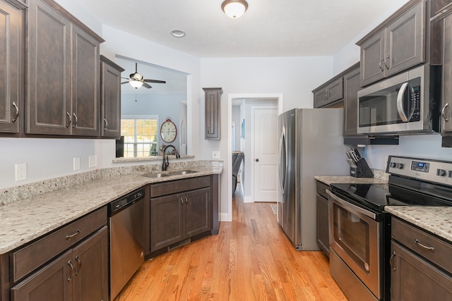 kitchen with ceiling fan, light stone countertops, light wood-type flooring, sink, and stainless steel appliances