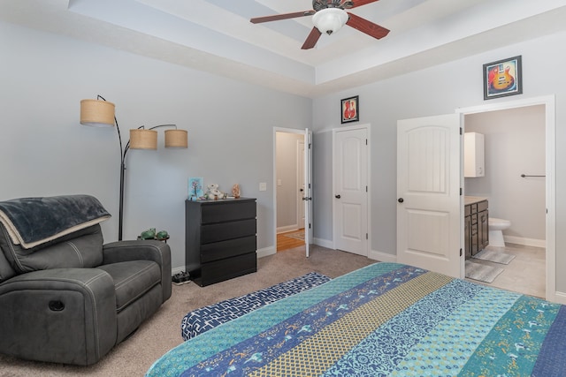 bedroom featuring light carpet, ensuite bathroom, a tray ceiling, and ceiling fan