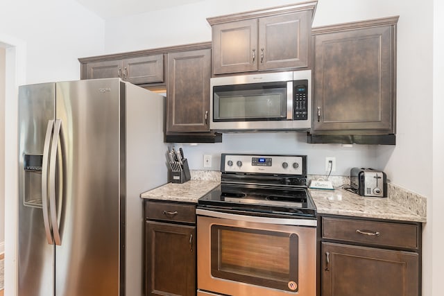 kitchen with appliances with stainless steel finishes, dark brown cabinetry, and light stone countertops