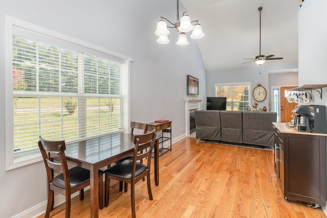 dining area featuring light hardwood / wood-style flooring, high vaulted ceiling, and ceiling fan with notable chandelier