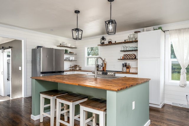 kitchen with a center island with sink, sink, a barn door, stainless steel fridge, and butcher block countertops