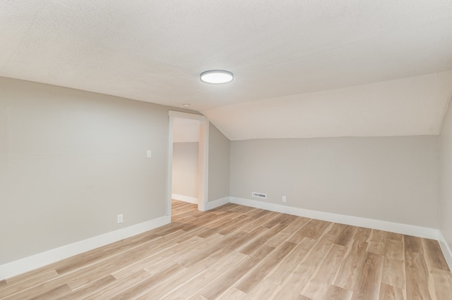 additional living space with light hardwood / wood-style floors, lofted ceiling, and a textured ceiling