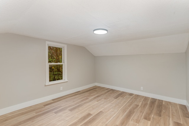 additional living space featuring a textured ceiling, vaulted ceiling, and light wood-type flooring