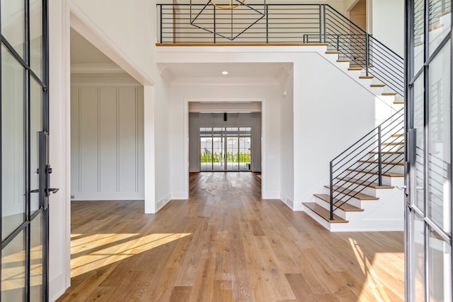 foyer with crown molding, a towering ceiling, and light hardwood / wood-style floors