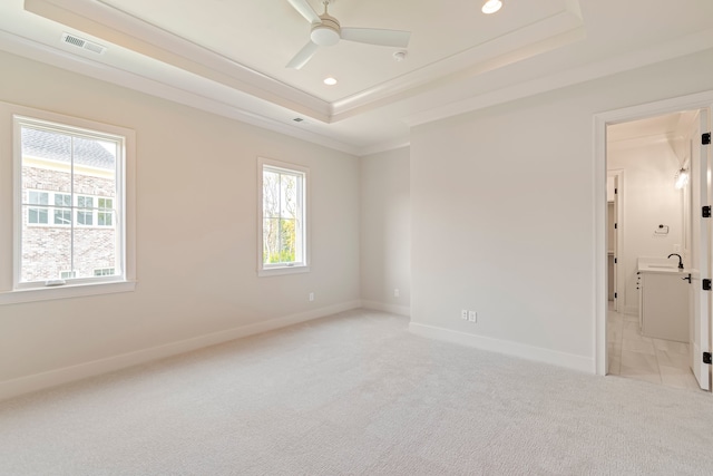 carpeted empty room with a raised ceiling, ornamental molding, a healthy amount of sunlight, and ceiling fan