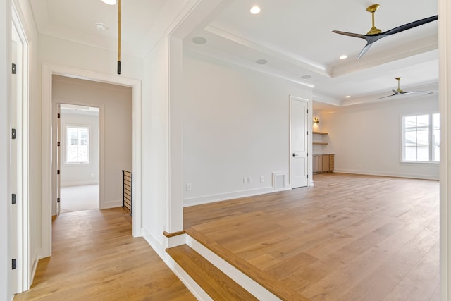 interior space featuring a raised ceiling, ceiling fan, ornamental molding, and light wood-type flooring