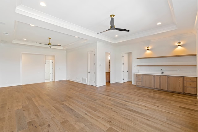 unfurnished living room featuring a raised ceiling, ceiling fan, and light hardwood / wood-style floors