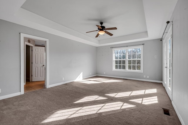 empty room with ceiling fan, a raised ceiling, and light colored carpet