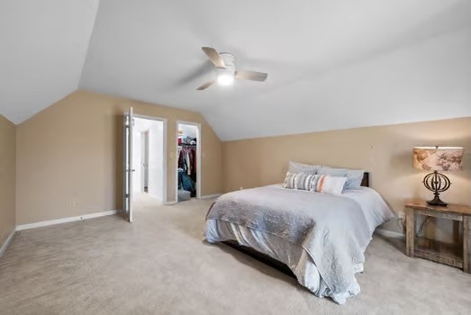 bedroom with a walk in closet, ceiling fan, vaulted ceiling, a closet, and light colored carpet