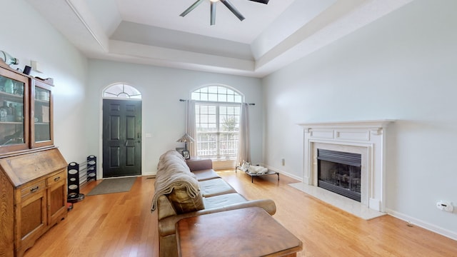 living room featuring a high end fireplace, a tray ceiling, light wood-type flooring, and ceiling fan