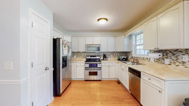 kitchen featuring tasteful backsplash, sink, a textured ceiling, light hardwood / wood-style floors, and stainless steel appliances