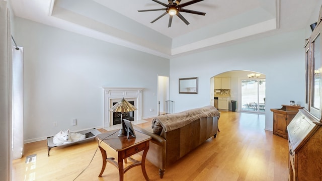 living room featuring a towering ceiling, a tray ceiling, light wood-type flooring, and ceiling fan