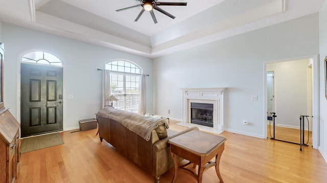 living room with ceiling fan, a raised ceiling, light wood-type flooring, and a fireplace