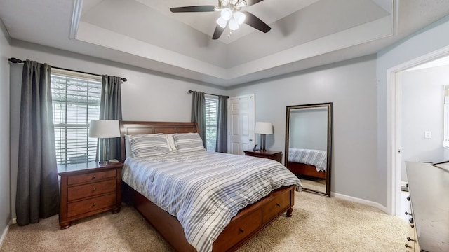 bedroom with light colored carpet, a tray ceiling, and ceiling fan