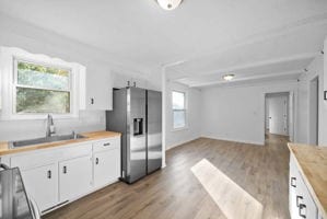 kitchen with stainless steel fridge, white cabinets, wood counters, light wood-type flooring, and sink