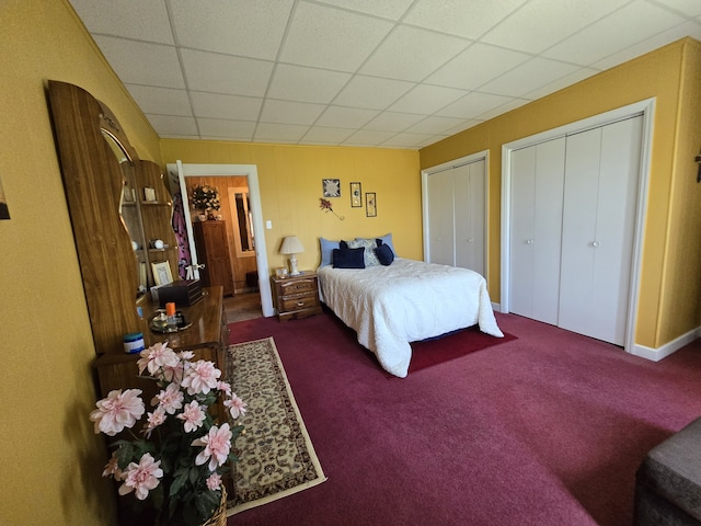 bedroom with a drop ceiling, multiple closets, and dark colored carpet