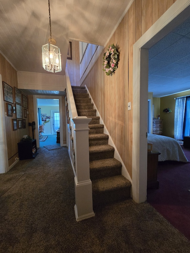 staircase with a notable chandelier, carpet, and wooden walls