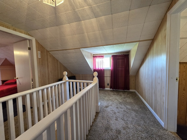 hall featuring wood walls, carpet flooring, and lofted ceiling