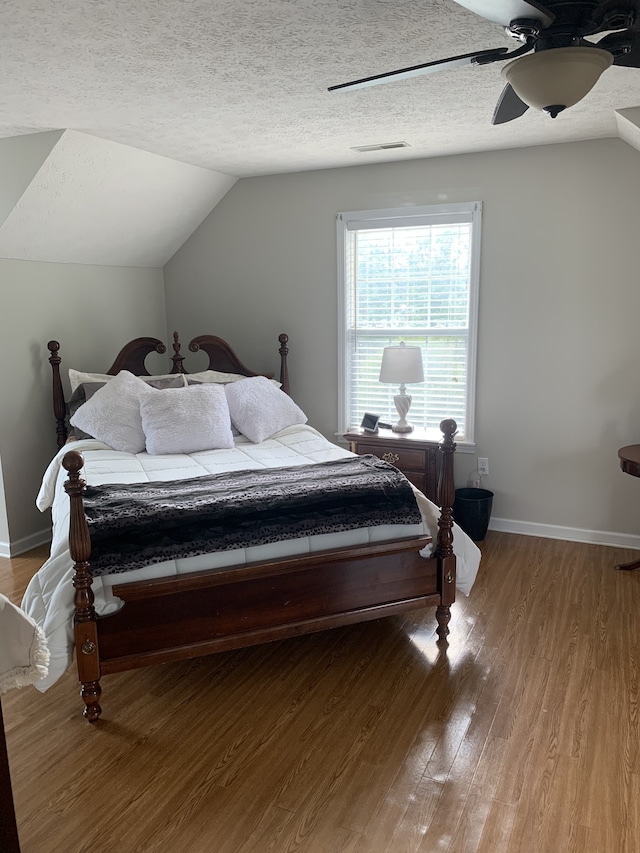 bedroom featuring lofted ceiling, hardwood / wood-style floors, a textured ceiling, and ceiling fan