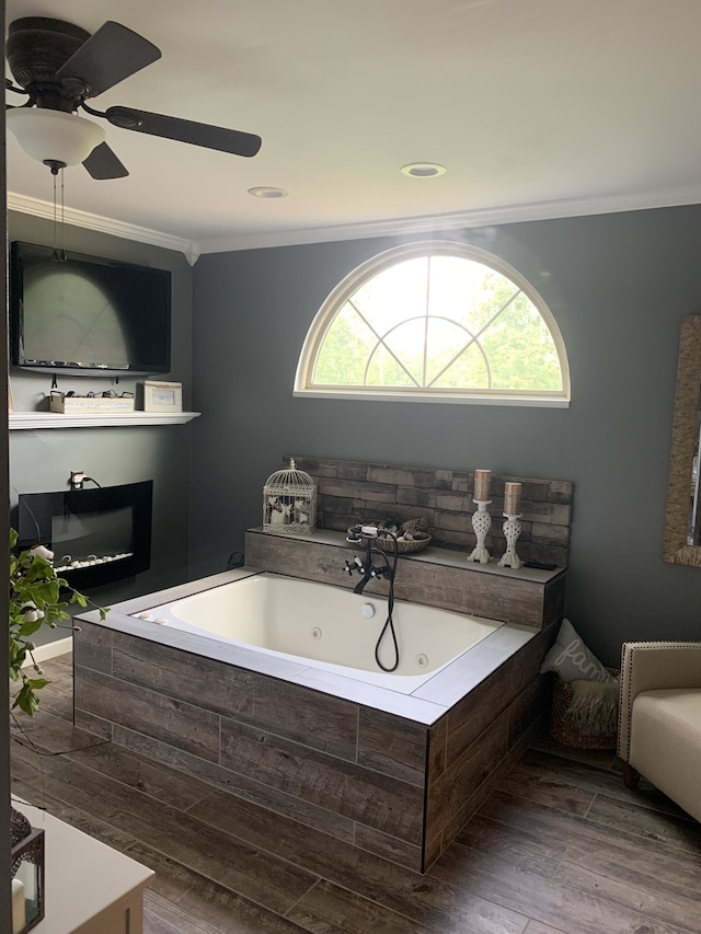 bathroom with hardwood / wood-style floors, crown molding, tiled tub, and ceiling fan