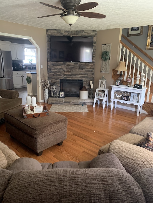 living room with light hardwood / wood-style floors, a textured ceiling, and ceiling fan