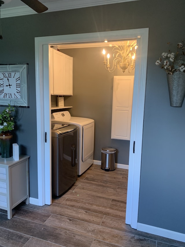 laundry area featuring wood-type flooring, crown molding, cabinets, washing machine and clothes dryer, and ceiling fan with notable chandelier