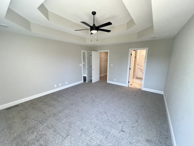 unfurnished bedroom featuring a closet, a tray ceiling, a spacious closet, carpet floors, and ceiling fan