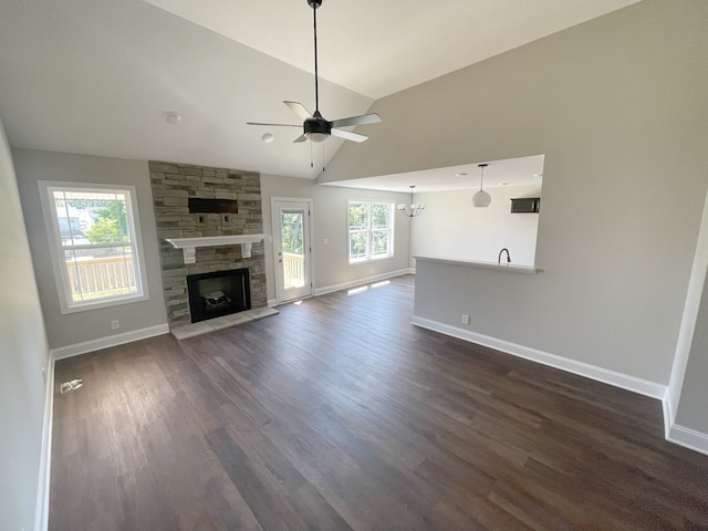 unfurnished living room with dark wood-type flooring, ceiling fan with notable chandelier, a fireplace, and high vaulted ceiling