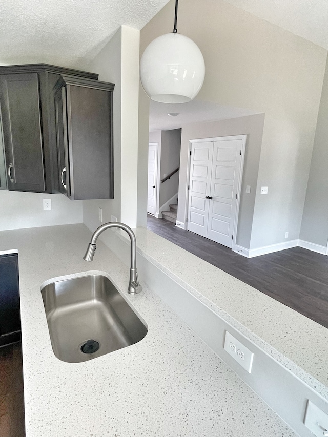 kitchen featuring sink, dark brown cabinets, dark hardwood / wood-style flooring, decorative light fixtures, and light stone counters