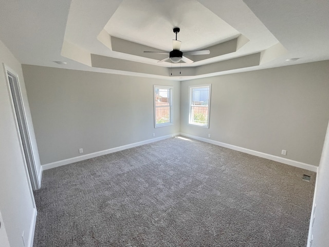 empty room with ceiling fan, carpet floors, and a raised ceiling