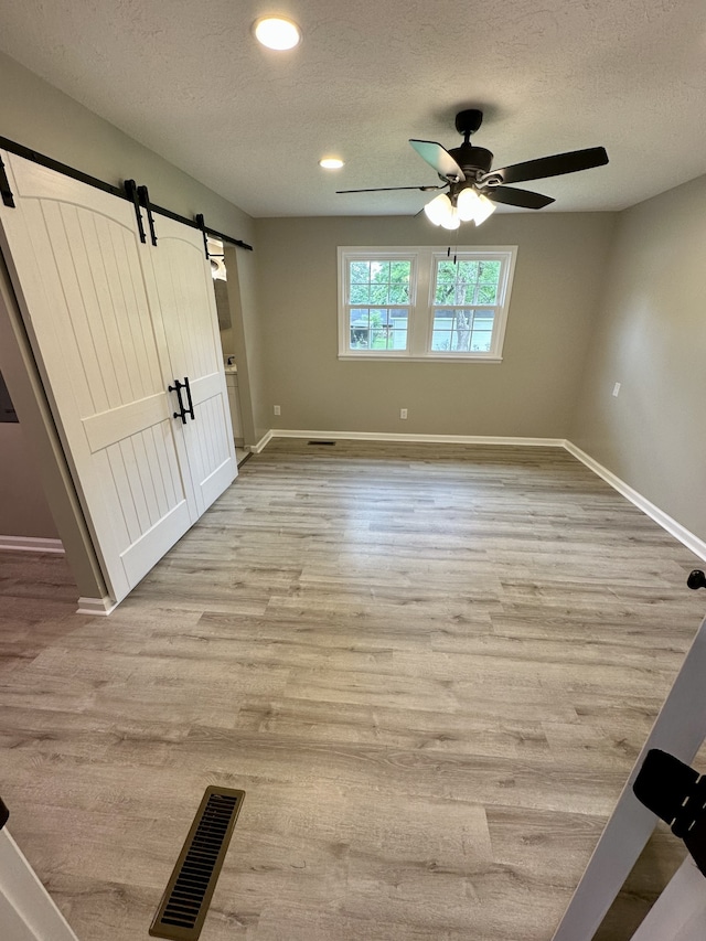 spare room featuring a barn door, ceiling fan, light hardwood / wood-style floors, and a textured ceiling