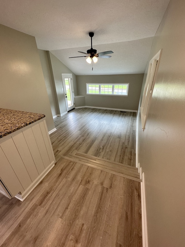 unfurnished living room with wood-type flooring, a textured ceiling, ceiling fan, and lofted ceiling