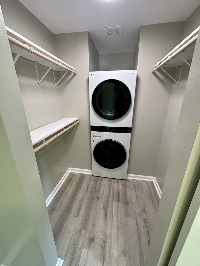 walk in closet with stacked washer and dryer and light hardwood / wood-style flooring