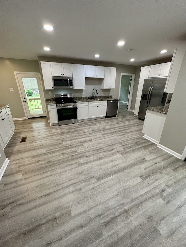 kitchen with light wood-type flooring, dark stone counters, stainless steel appliances, sink, and white cabinetry