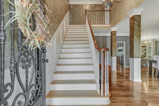 stairway with ornate columns, a notable chandelier, wood-type flooring, and ornamental molding