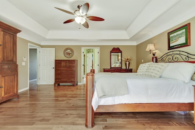 bedroom with light hardwood / wood-style flooring, ornamental molding, a tray ceiling, and ceiling fan