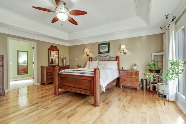 bedroom with ceiling fan, crown molding, a tray ceiling, and light wood-type flooring