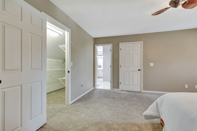 bedroom featuring a spacious closet, light colored carpet, a closet, and ceiling fan