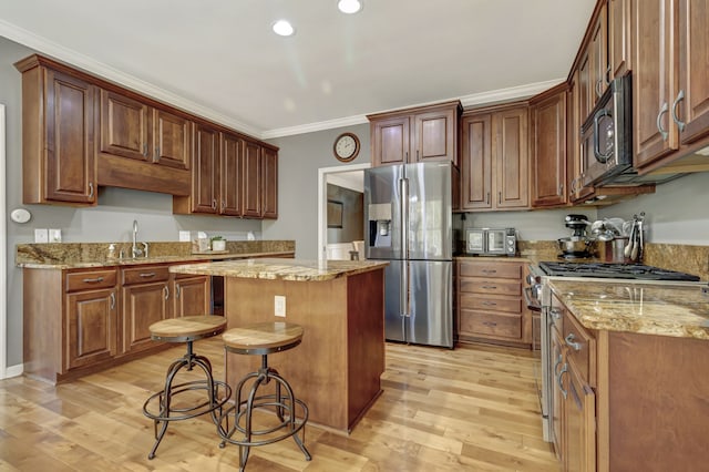 kitchen with a kitchen island, light stone countertops, stainless steel appliances, and light hardwood / wood-style floors