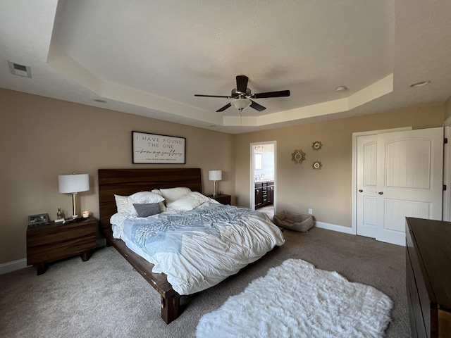 carpeted bedroom with ensuite bathroom, ceiling fan, and a tray ceiling