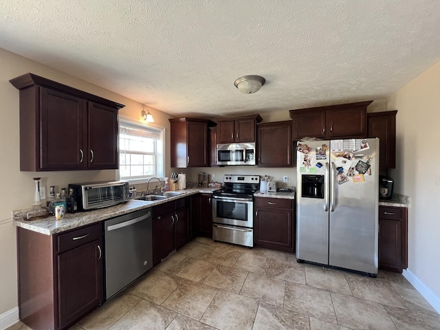 kitchen with stainless steel appliances, a textured ceiling, light stone counters, dark brown cabinetry, and sink