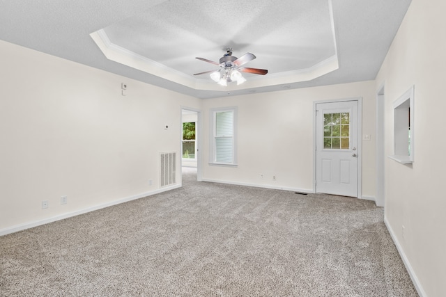 carpeted empty room with ceiling fan, a textured ceiling, a tray ceiling, and plenty of natural light