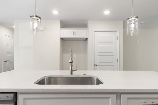 kitchen featuring light stone countertops, sink, white cabinetry, and pendant lighting