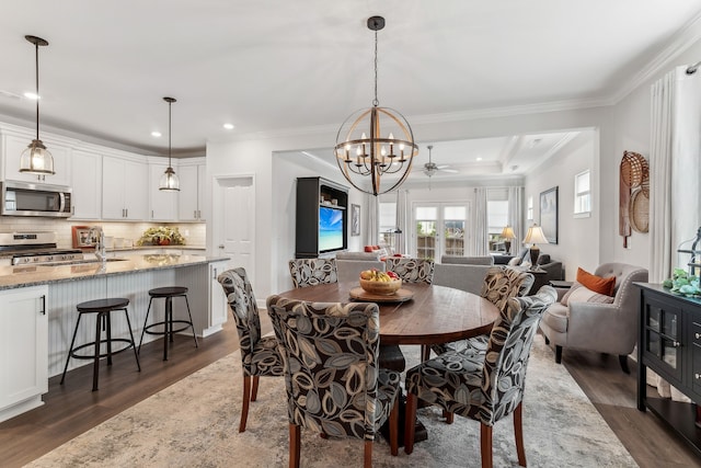 dining space with sink, dark wood-type flooring, crown molding, and ceiling fan with notable chandelier