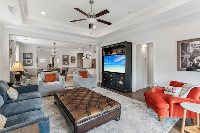 living room with crown molding, ceiling fan, wood-type flooring, and a raised ceiling