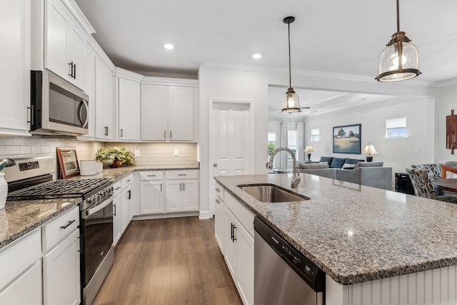 kitchen with an island with sink, sink, white cabinets, pendant lighting, and appliances with stainless steel finishes